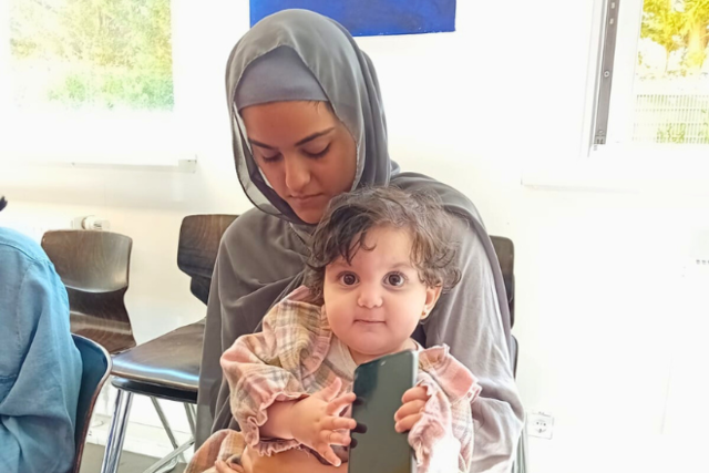eine junge muslimische Frau sitzt mit ihrem jungen Kind auf dem Schoß