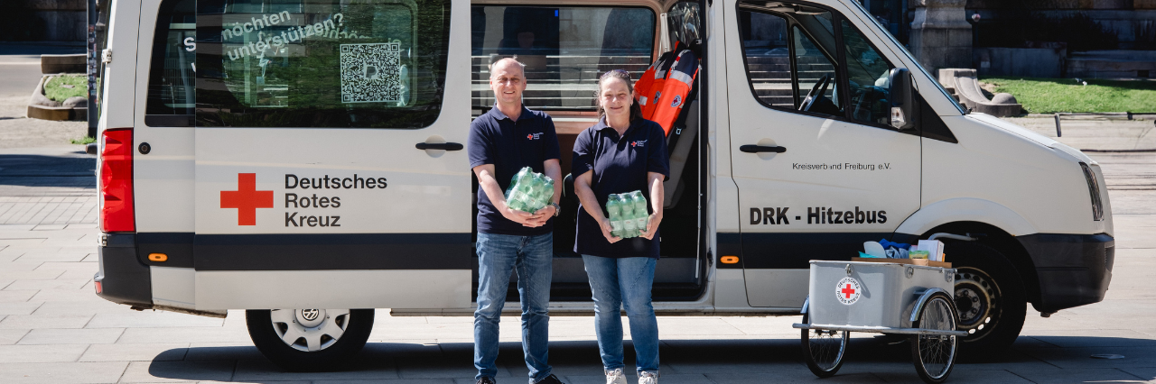 zwei Mitarbeitende stehen mit dem DRK-Hitzebus in Freiburg