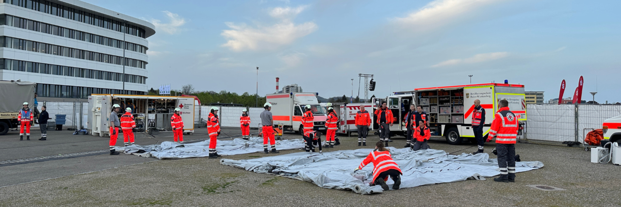 mehrere Helferinnen und Helfer in Einsatzkleidung bauen ein Versorgungszelt auf