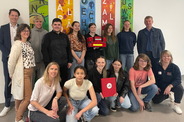 eine Gruppe Schüler steht mit einem Erste-Hilfe-Rucksack vor der Kamera und lächelt