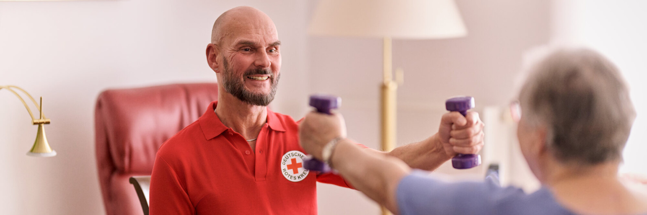 ein lächelnder Physiotherapeut macht mit einer älteren Damen gemeinsam Sport