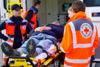 drei Helfer stehen in Einsatzkleidung um eine Trage, auf der ein Patient liegt