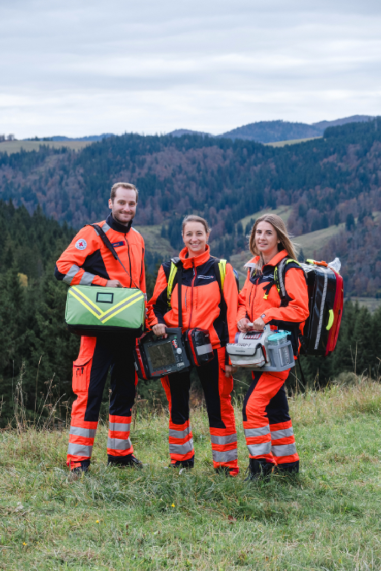 drei junge Notfallsanitäter:innen stehen in Dienstkleidung vor einem Schwarzwaldpanorama