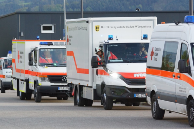mehrere Fahrzeuge des Bevölkerungsschutzes fahren hintereinander, aus einem Fahrzeug lehnt sich ein ehrenamtlicher Helfer in Uniform