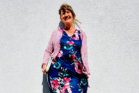 eine Frau steht in einem bunten Kleid vor einer Wand und lächelt in die Kamera